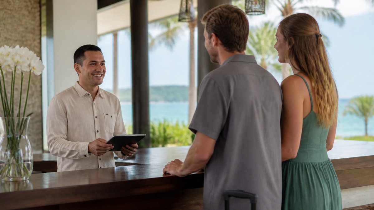 Luxury hotel concierge or property manager at an elegant front desk, smiling while assisting guests with digital check-in on a tablet, collecting contact information with professional courtesy in a high-end coastal property setting