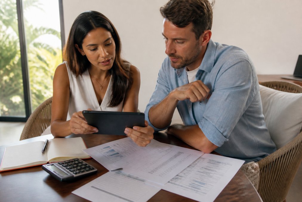Property manager and remote owner reviewing rental income and fee statements on a tablet in a modern office setting