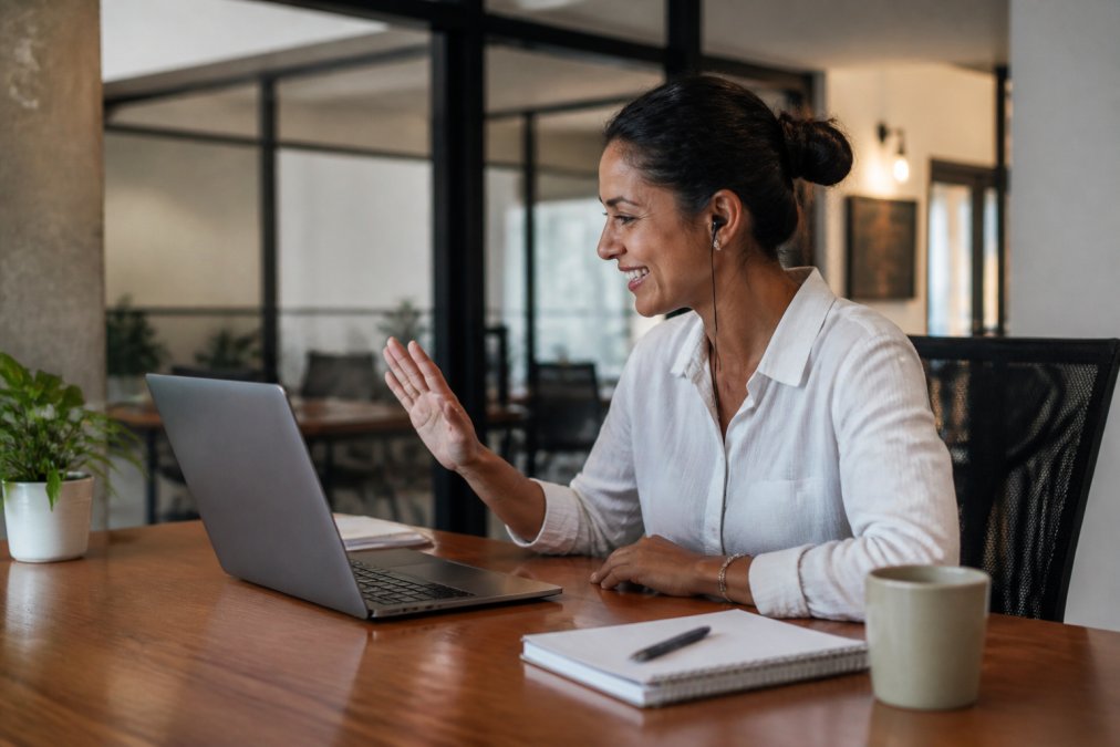 Property manager or concierge team member communicating with guest via video call on laptop in modern office setting, showing attentive service and professional hospitality with warm lighting